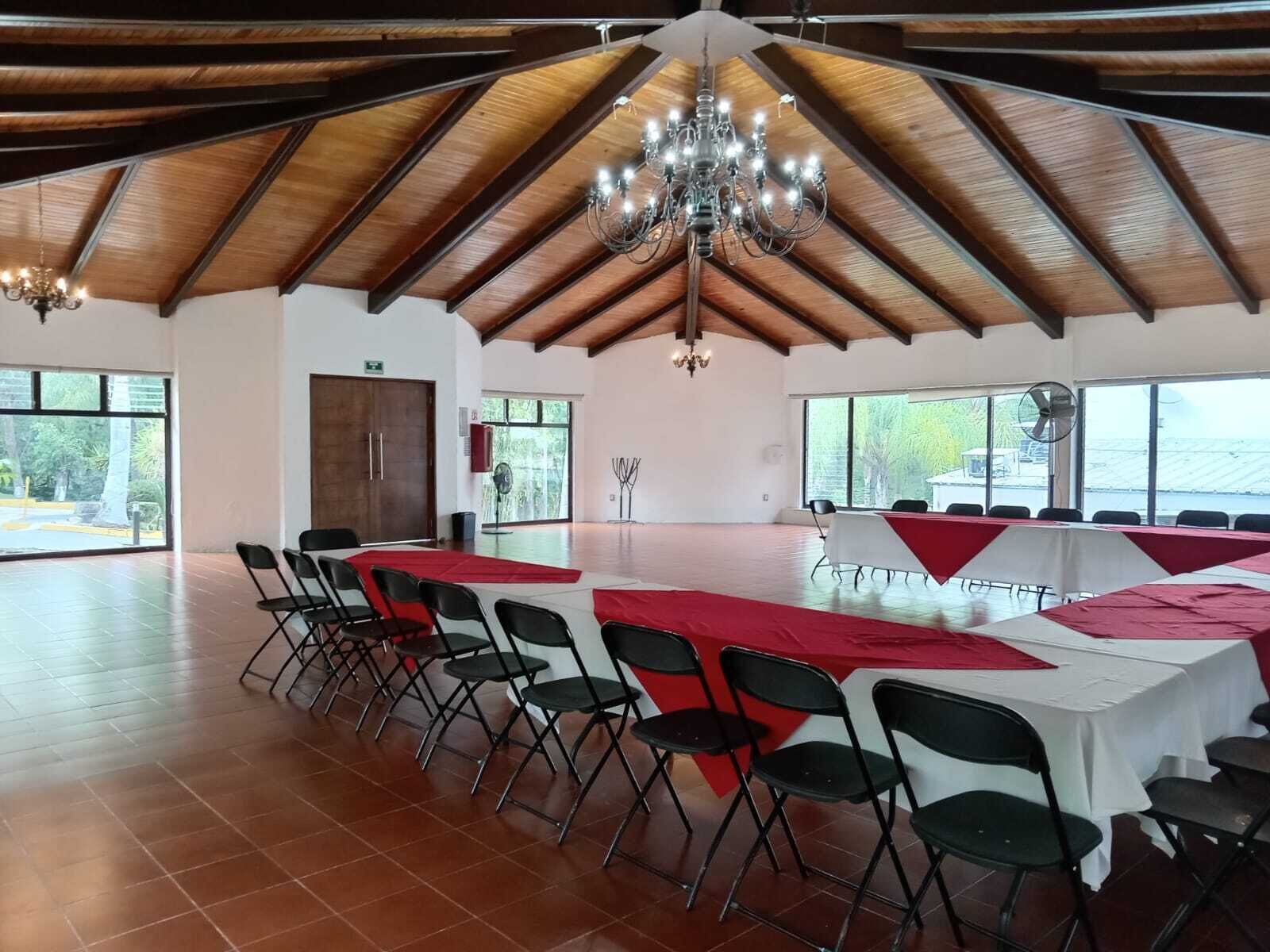 Un hallo espacioso con techo alto y vigas de madera, ventanas grandes y un candelabro.