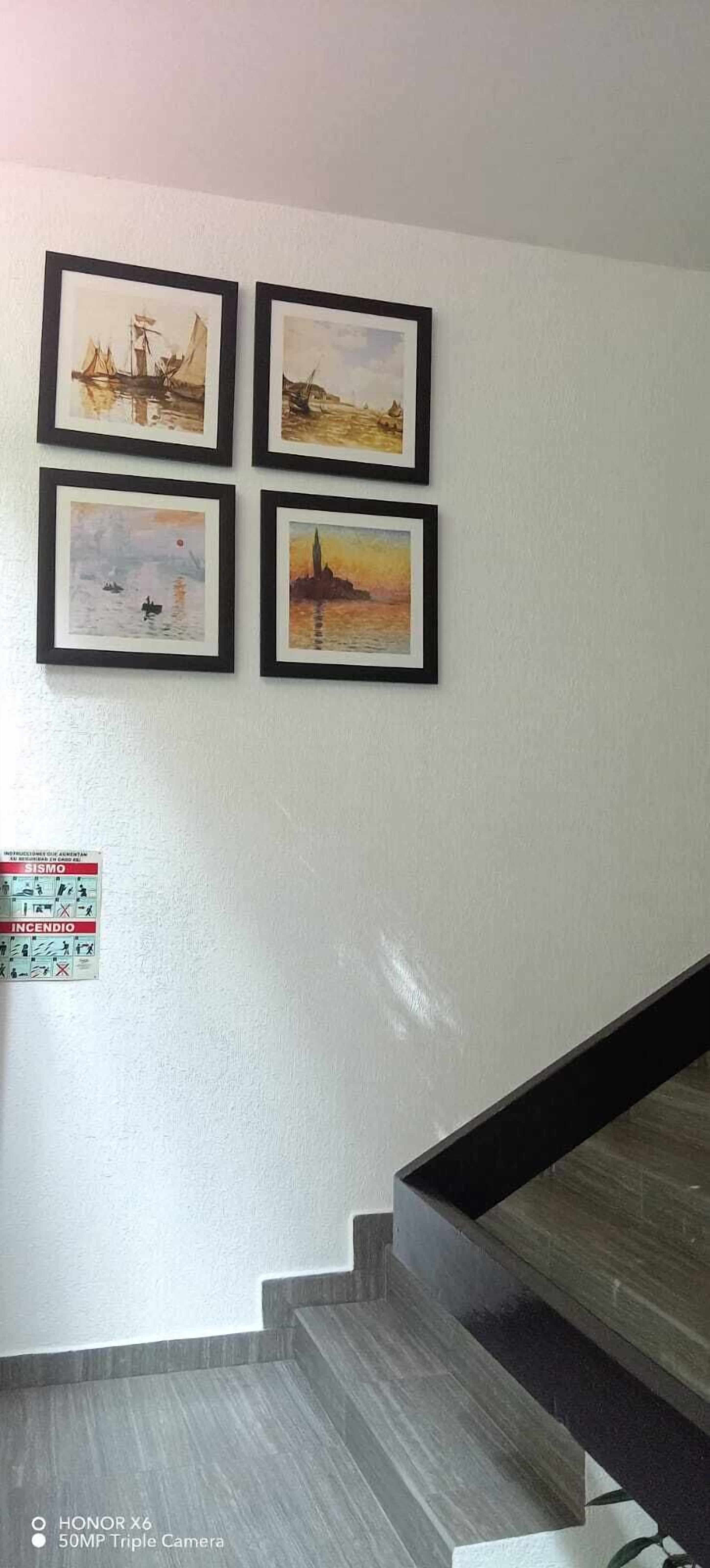 A staircase with a handrail and a wall with four framed paintings.