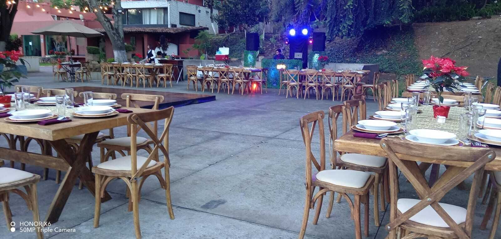 An outdoor dining area with wooden tables and chairs, arranged for a formal event.