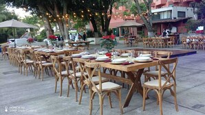 An outdoor dining area with wooden tables and chairs, string lights, and a stage with blue lighting. - HOTEL PUNTA GALERIA (Morelia)