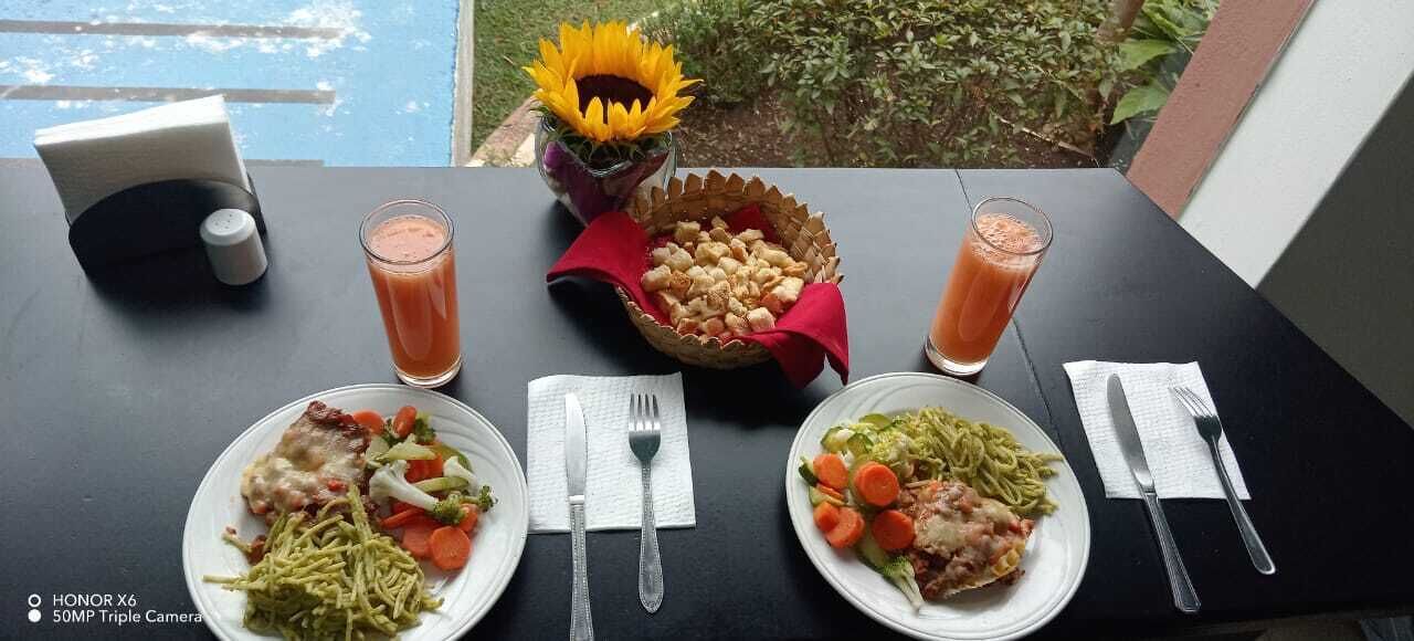 A table set with three plates of food, two glasses of juice, and a vase with a sunflower.