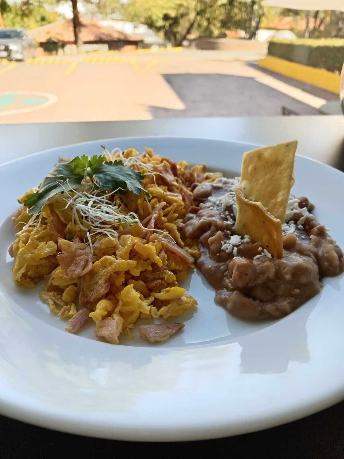 En tallerken med mad, der indeholder røræg, genopvarmede bønner og en tortilla-chip.