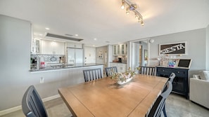 Een moderne keuken met witte kastjes, een centraal eiland en een eetgedeelte met een houten tafel en stoelen.