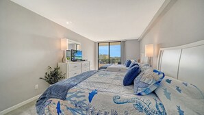 A bedroom with a large bed, a dresser, a mirror, and a view of the city. - The Anchorage - Unit 607 (Siesta Key)
