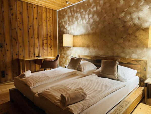 A double bed with white linens and two pillows, a wooden desk with a chair, and a wall with a textured pattern. - Hotel Nest (Berlin)