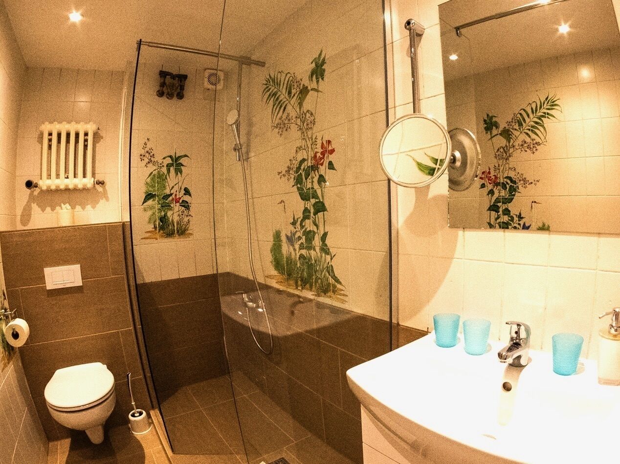 A bathroom with a glass-enclosed shower, a toilet, and a sink with blue cups.