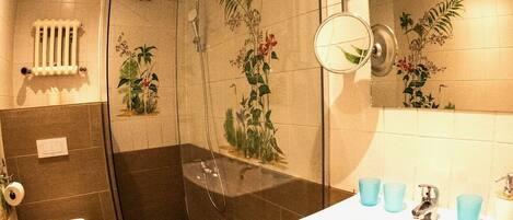 A bathroom with a glass-enclosed shower, a toilet, and a sink with blue cups.