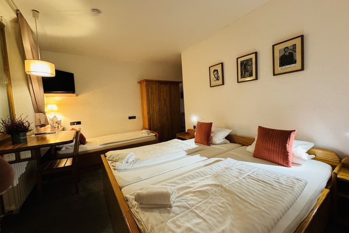 Habitación de hotel con dos camas individuales, un armario de madera, un escritorio con lámpara y un espejo.