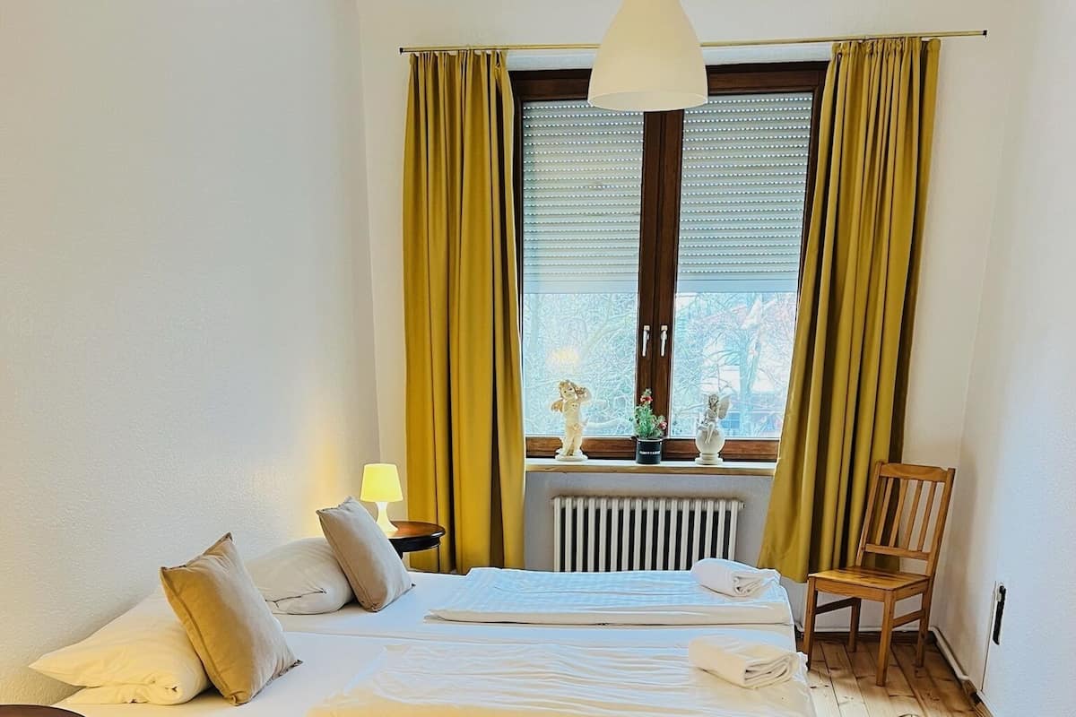 Un dormitorio con cama, una silla, una lámpara y una ventana con cortinas.