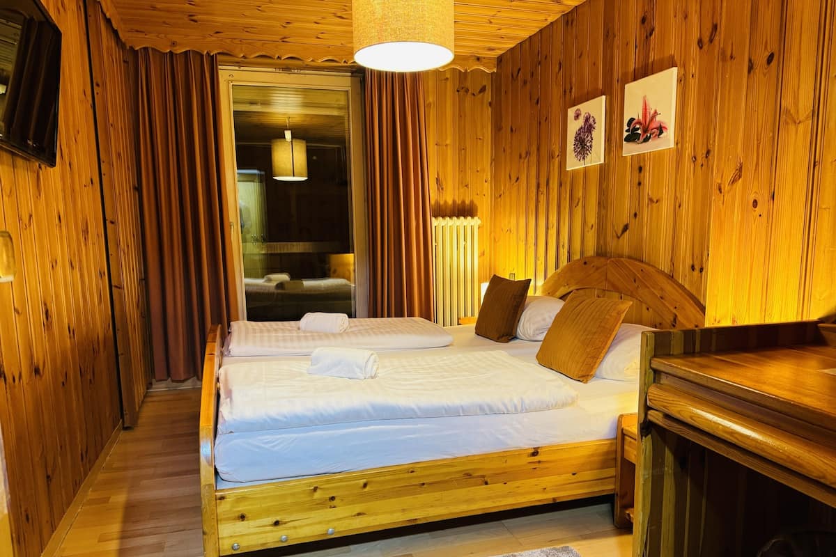Una habitación con paneles de madera, dos camas, un escritorio de madera y un ventanal con cortinas.