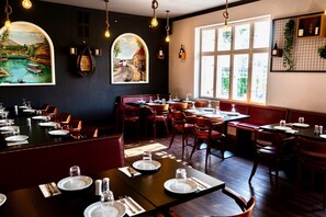 Un restaurant doté de nombreuses tables et de coins repas, de grandes fenêtres laissant entrer la lumière naturelle et d’œuvres d’art accrochées aux murs.
