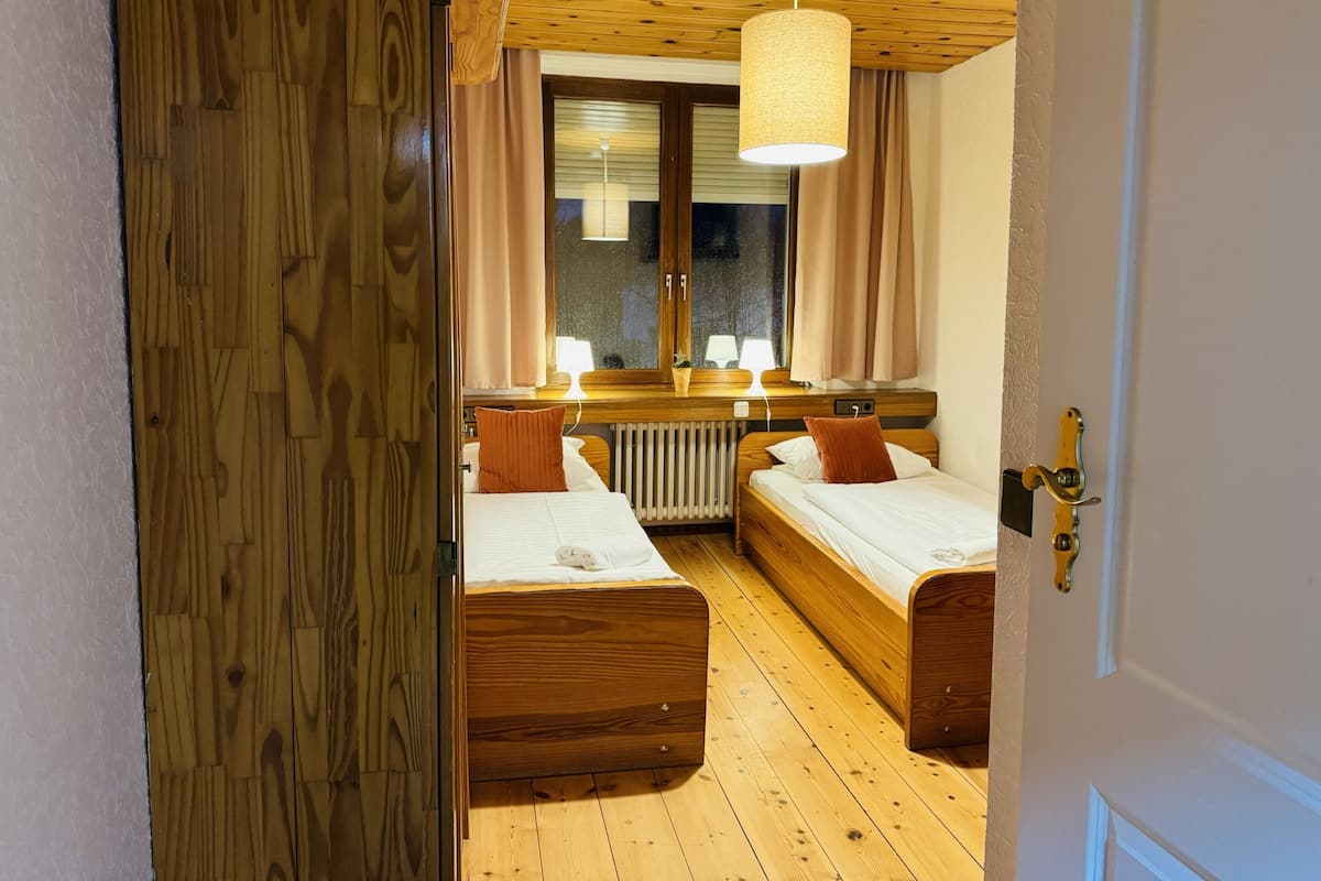 Una habitación con dos camas de madera, una ventana con cortinas, una lámpara colgante y un radiador.