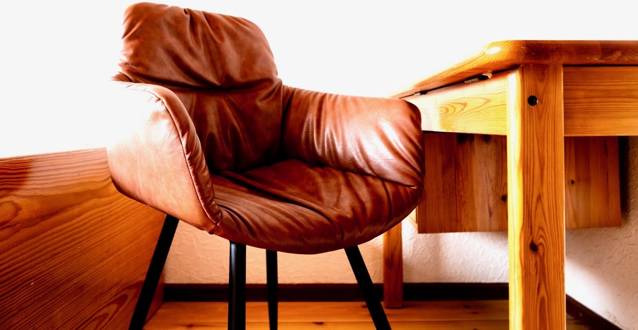 A brown leather chair with a high backrest, positioned next to a wooden desk with a drawer.
