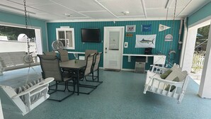 A covered outdoor area with a table and chairs, a hanging swing, and a door leading to another room. - 3 Bedroom House near Old Town (Bay St. Louis)