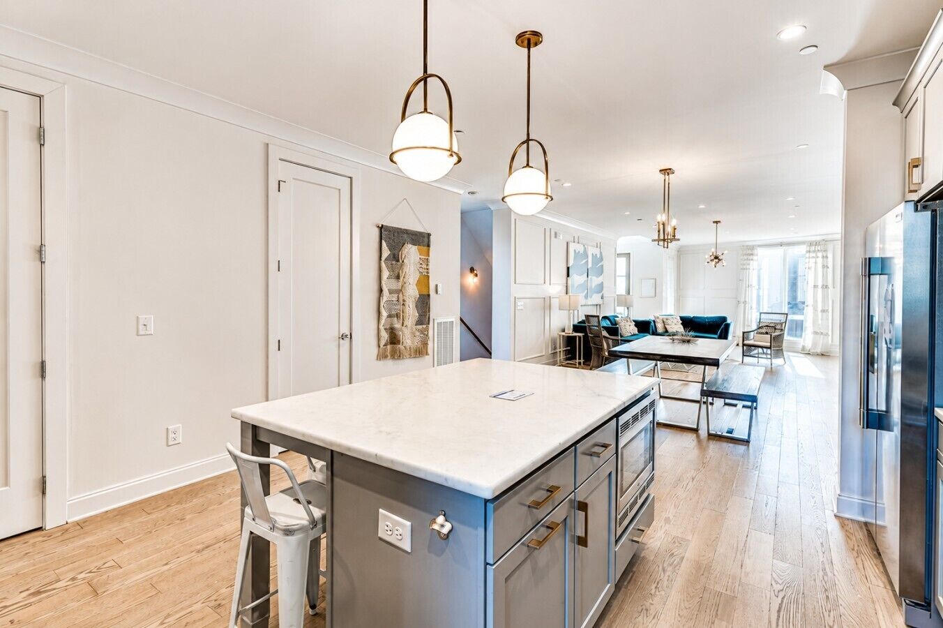 A modern kitchen with a large island, pendant lighting, and a view into the dining area.