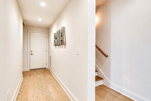 A hallway with a wooden floor, a white door, and a staircase with a wooden handrail.