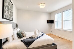 Habitación de hotel con una cama, un televisor de pantalla plana montado en la pared y una ventana con persianas.