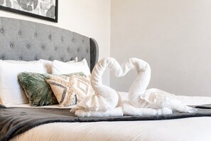A bed with a grey upholstered headboard, white bedding, and a decorative pillow with a geometric pattern. - 4BR townhome near The Gulch with rooftop skyline views (Nashville)