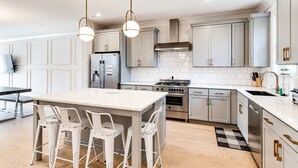 A modern kitchen with white cabinetry, a central island with chairs, stainless steel appliances, and pendant lighting. - 4BR townhome near The Gulch with rooftop skyline views (Nashville)