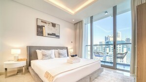 Et moderne hotelværelse med en stor seng, et sengebord, en lampe, udsigt over byen gennem store vinduer og et bybillede fra balkonen.