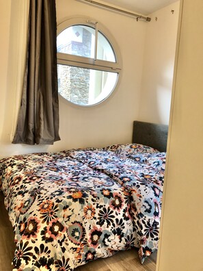 Cozy retreat with a single bed and round window offering a view of a nearby building.