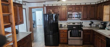 Una cocina con armarios de madera, un refrigerador negro, un microondas, un horno y un ventilador de techo.
