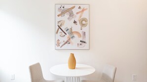 Una stanza minimalista con un tavolo bianco, due sedie e un vaso di legno.
