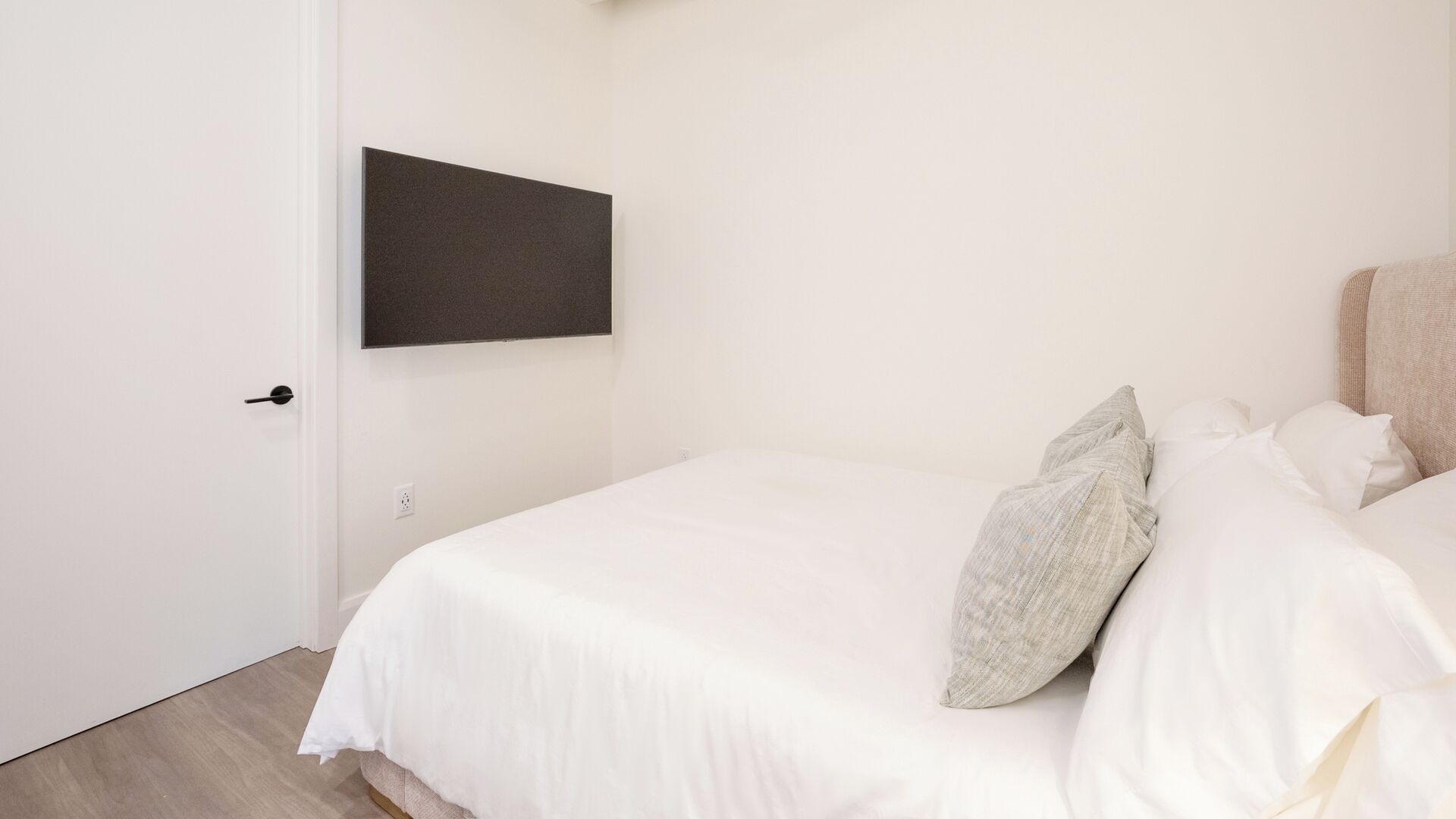 Een slaapkamer met een bed, kussens, een deur en een paneel aan de muur.
