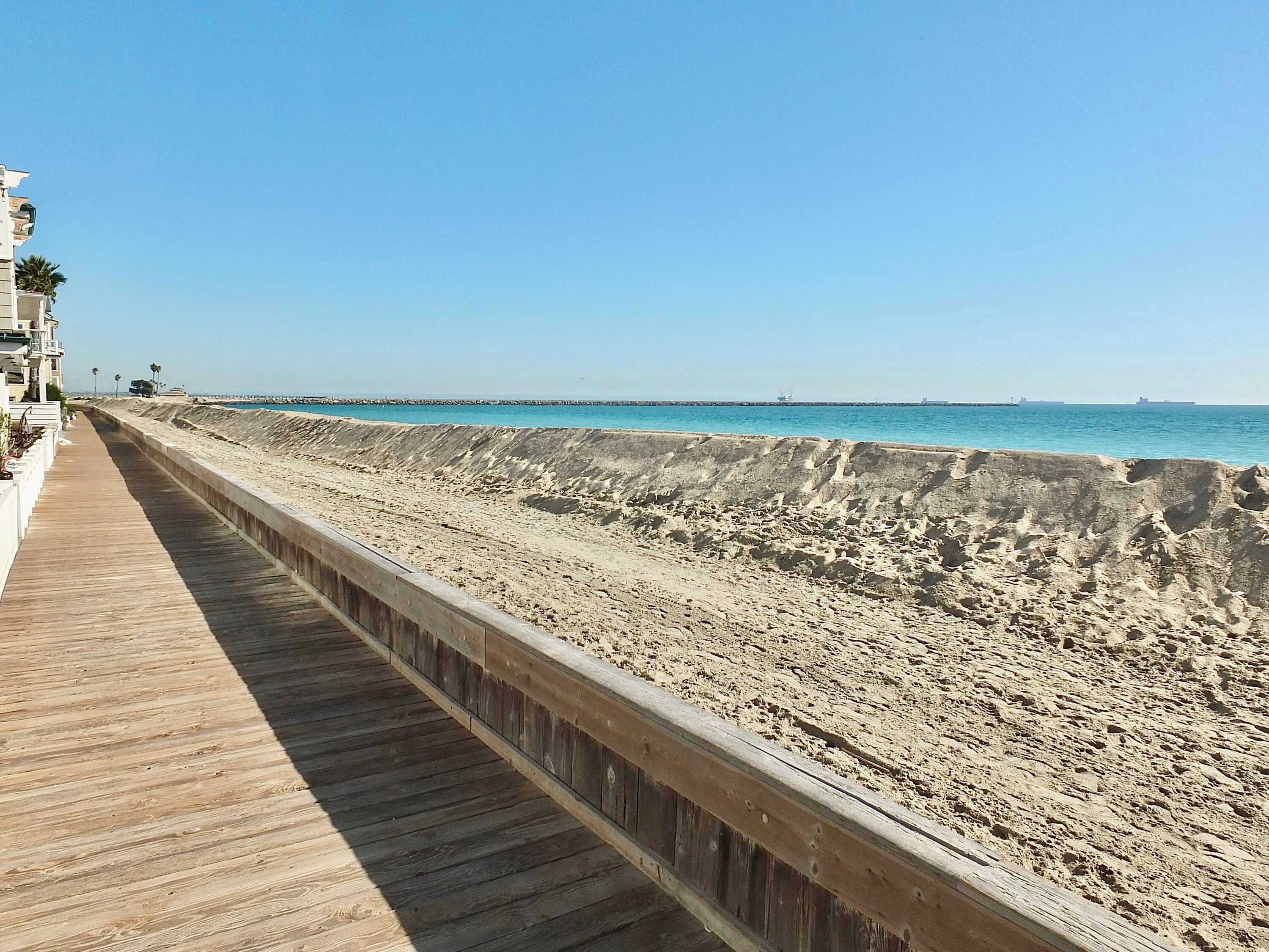 Een houten looppad langs een zandstrand met een helderblauwe lucht.