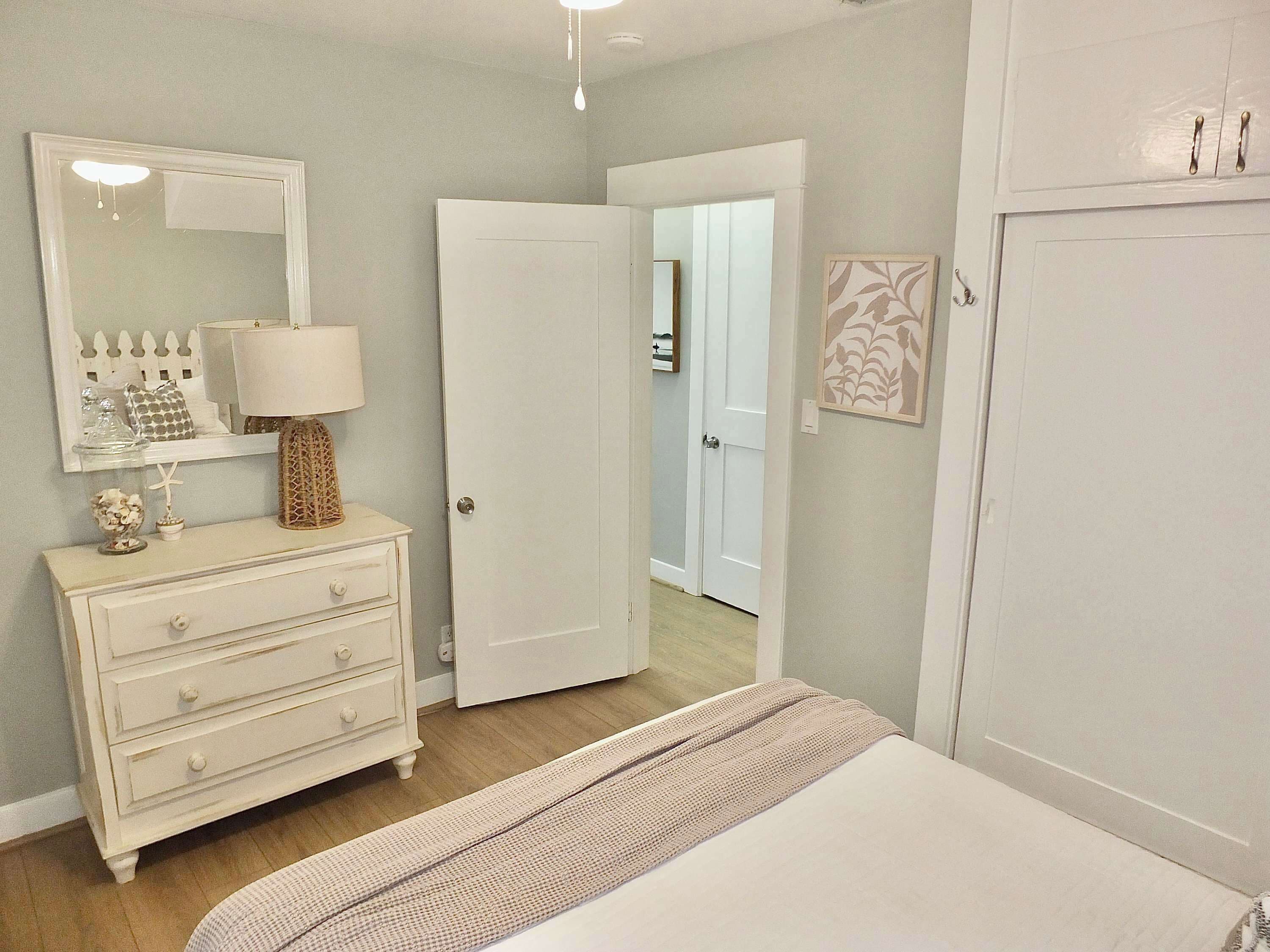Un dormitorio con cama, cómoda, espejo y puerta que da a otra habitación.
