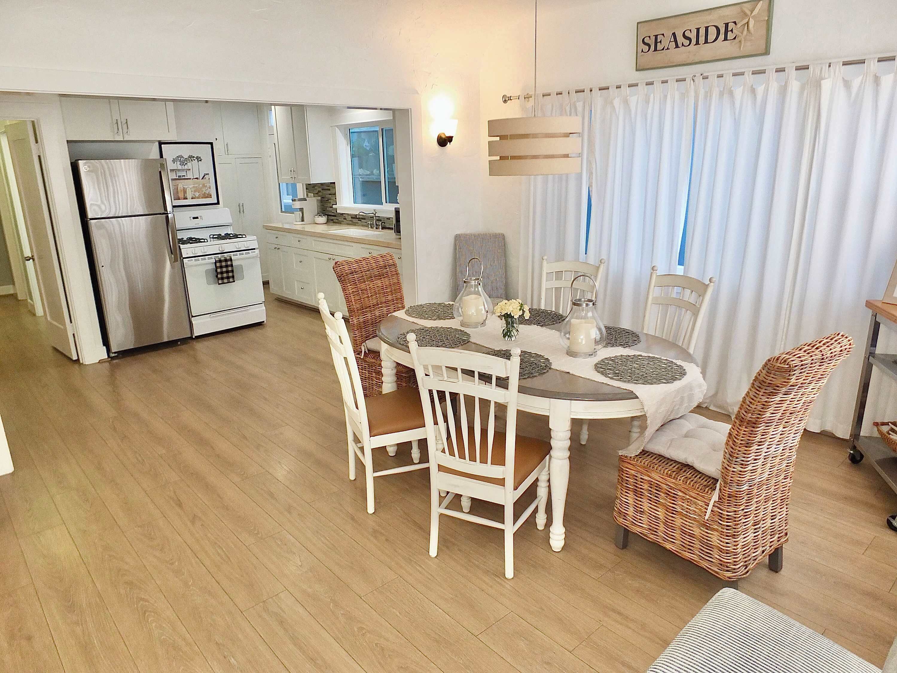 A modern kitchen with white cabinets, a stainless steel refrigerator, and a dining area with a round table and wicker chairs.