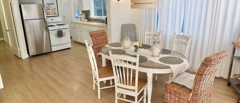 A modern kitchen with white cabinets, a stainless steel refrigerator, and a dining area with a round table and wicker chairs.