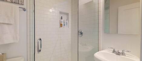 A modern bathroom with white tiled walls, a glass shower enclosure, a white sink, and a towel rack.