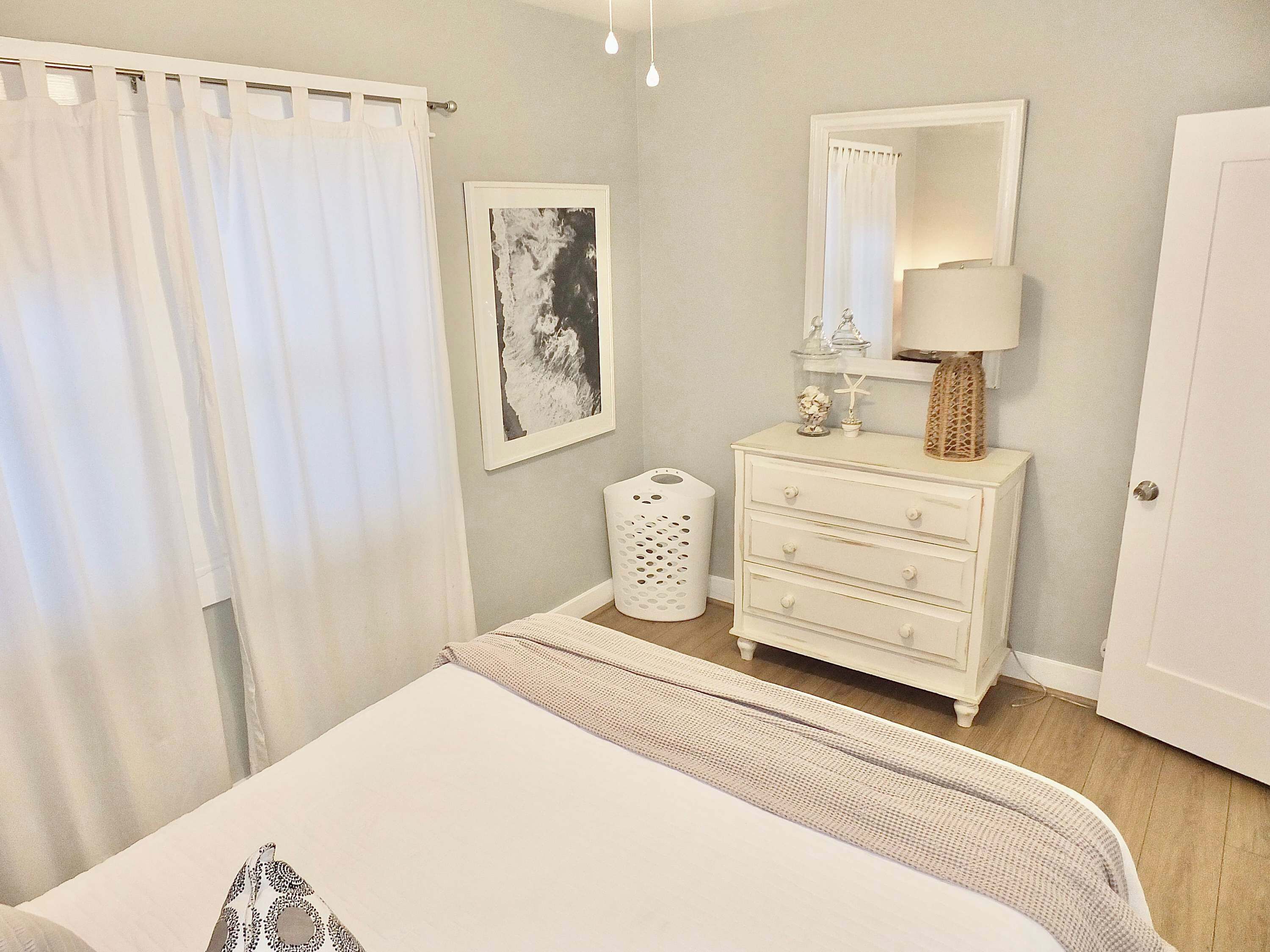 A bedroom with a bed, a dresser, a mirror, a lamp, and a wall-mounted picture.