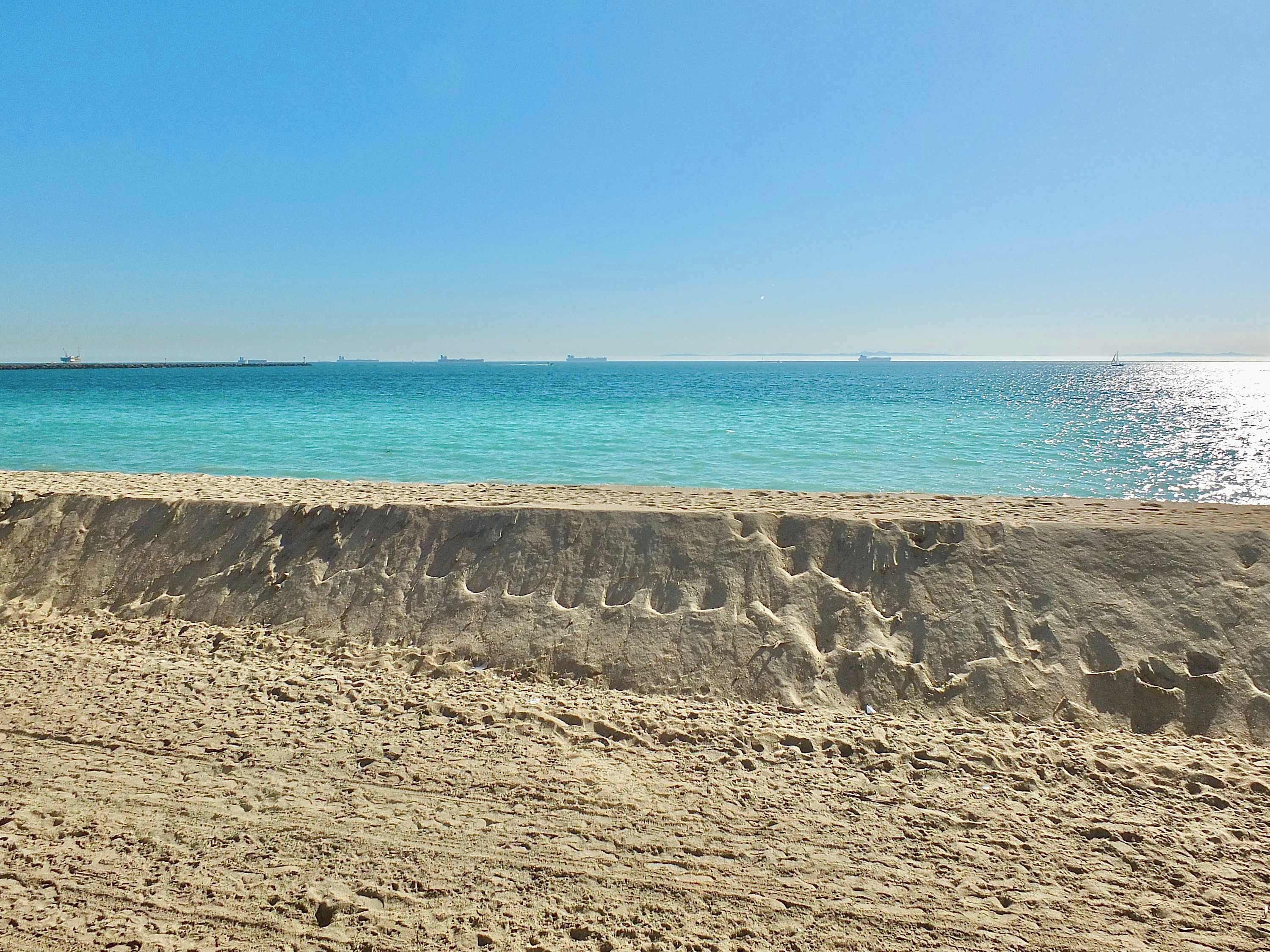 A sandy beach with a concrete barrier in the foreground and a calm sea in the background.