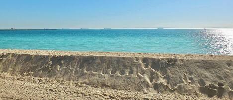 A sandy beach with a concrete barrier in the foreground and a calm sea in the background.