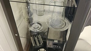 Eine Glastauschke mit verschiedenen Küchenutensilien, darunter Teekannen, Tassen und eine Kaffeemaschine.