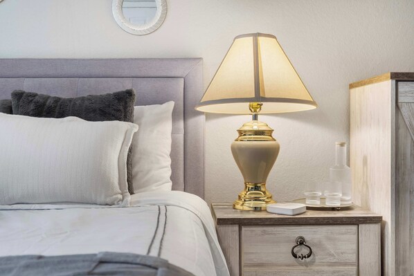 A neatly made bed with a grey headboard, a bedside lamp, a small wooden nightstand, and a mirror on the wall. - Catch the Sunrise - Branson Mo - Holiday Hills - 2bd Condo! (Branson)