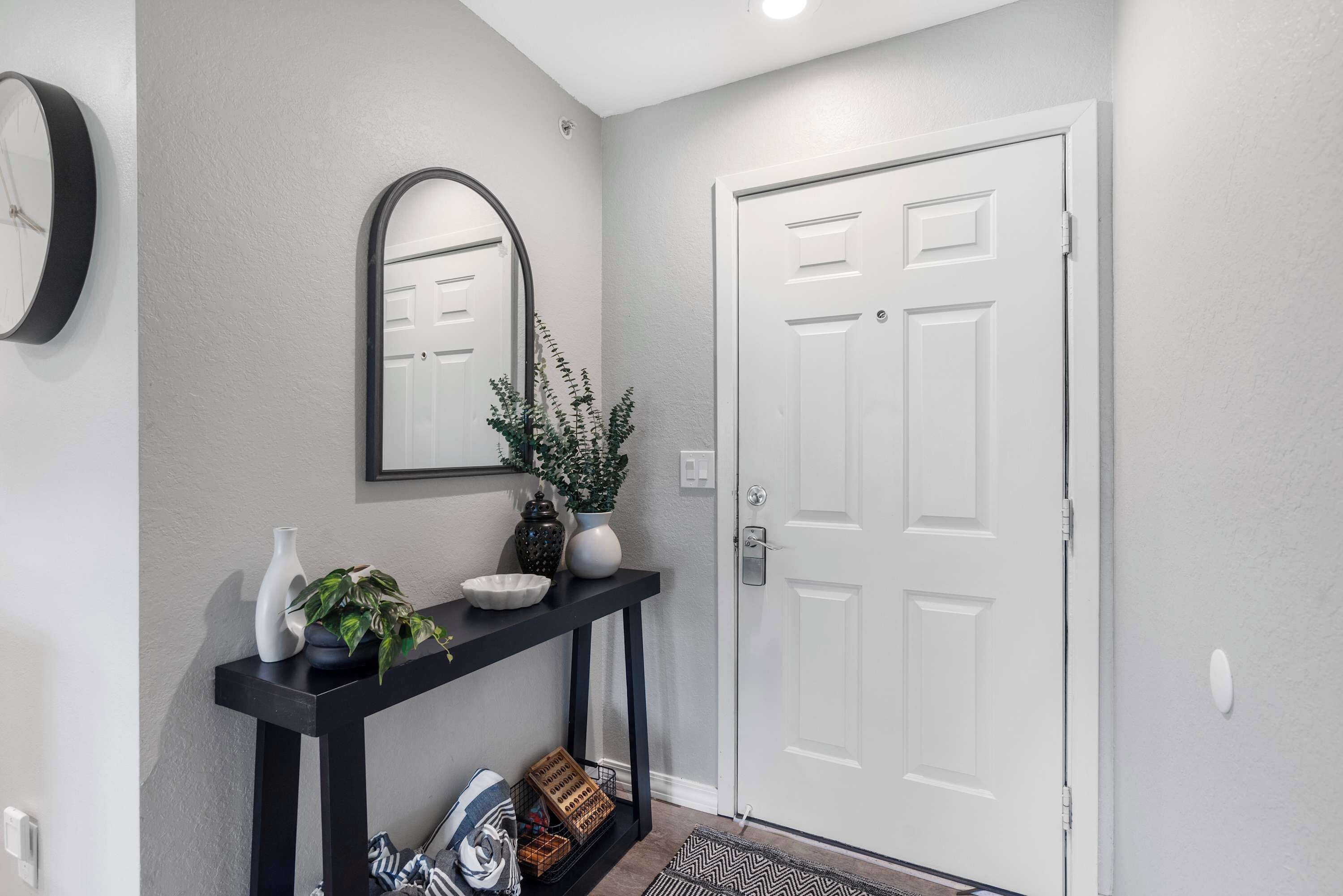 A hallway with a white door, a black console table with decorative items, and a mirror on the wall.