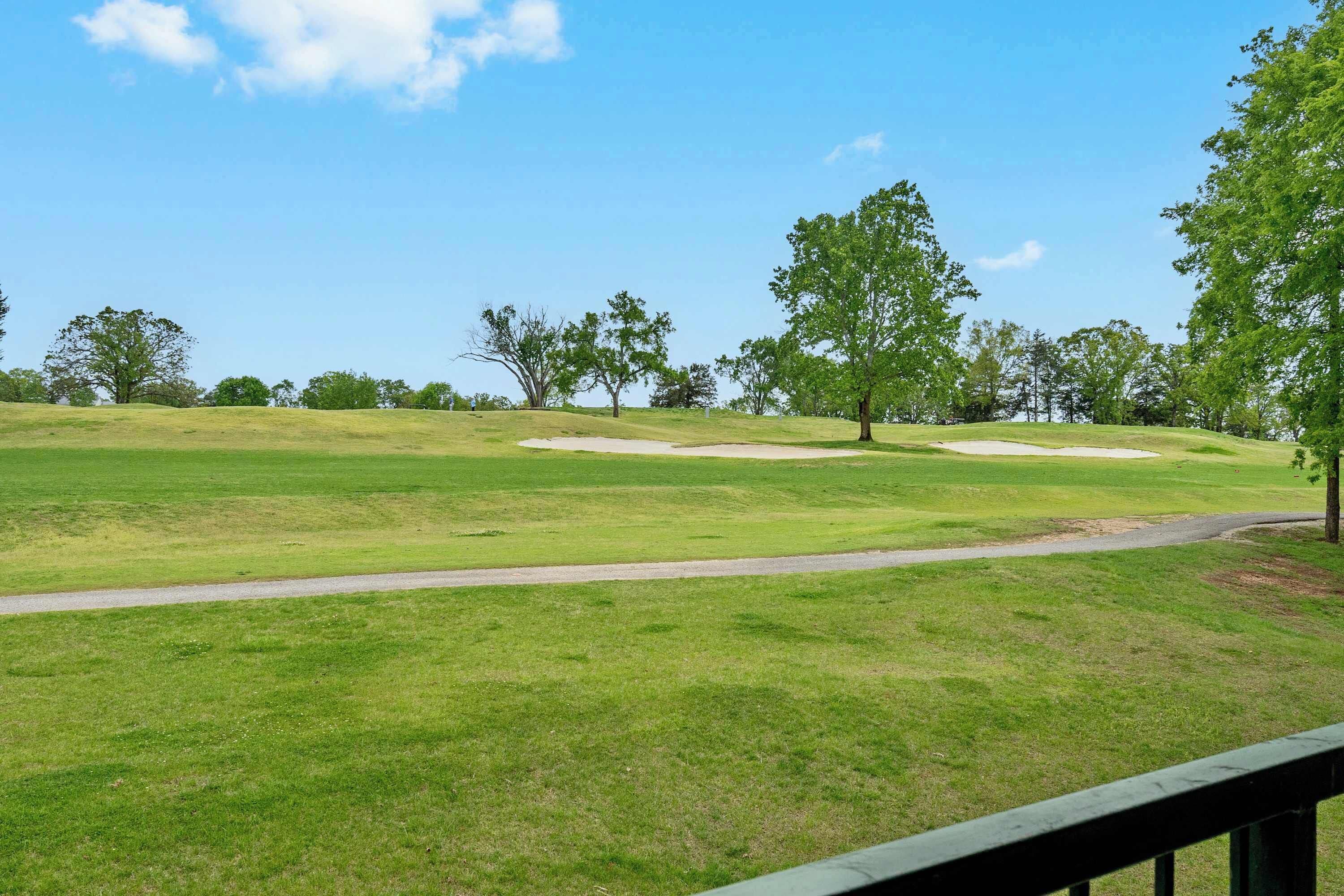 A golf course with a clear path, trees, and a well-maintained lawn.