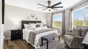 A bedroom with a bed, bedside tables, a bench, a chair, a ceiling fan, and large windows with curtains. - Catch the Sunrise - Branson Mo - Holiday Hills - 2bd Condo! (Branson)