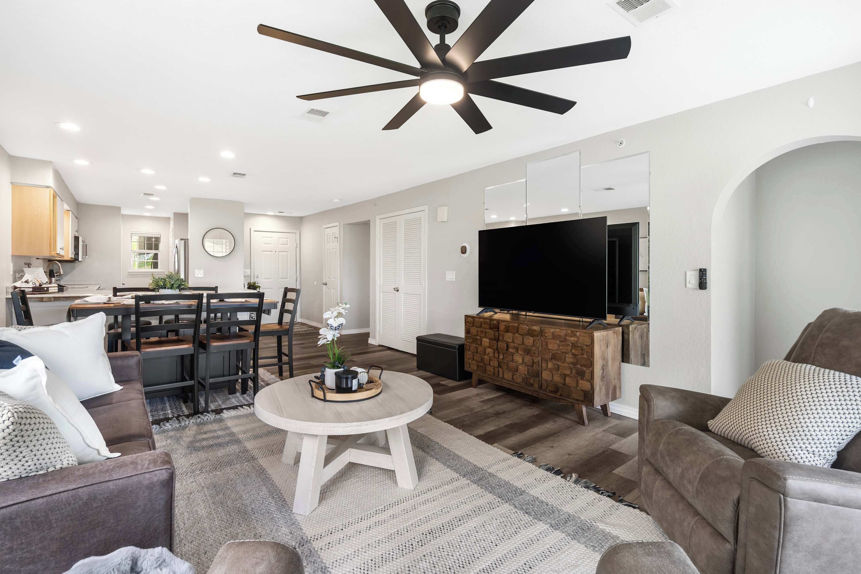 A modern living room with a ceiling fan, a TV, and a dining area with a table and chairs.