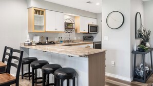 A modern kitchen with a central island, bar stools, and a dining area with a wooden table. - Catch the Sunrise - Branson Mo - Holiday Hills - 2bd Condo! (Branson)