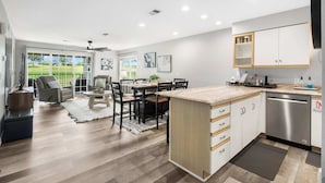 A modern kitchen with a dishwasher, white cabinets, and a dining area with a table and chairs. - Catch the Sunrise - Branson Mo - Holiday Hills - 2bd Condo! (Branson)