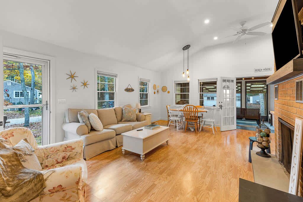 A spacious living room with a wooden floor, a white sofa, a dining table with chairs, and a fireplace.