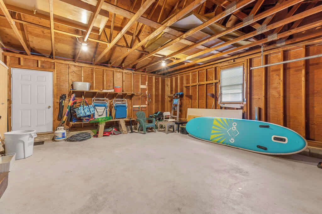 Une pièce avec un plafond en bois, une porte, une planche de surf bleue et divers objets disposés sur des étagères et sur le sol.