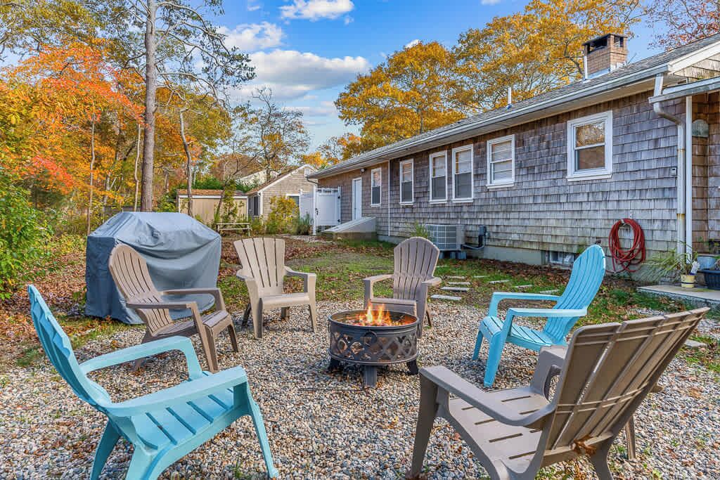 Un patio con sillas Adirondack, una chimenea y una zona de parrilla cubierta.