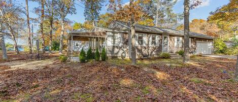 A rustic wooden house with a porch, surrounded by trees and a leaf-covered ground.