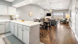 Cocina amplia con una isla central, comedor con sillas y sala de estar con televisor y asientos.