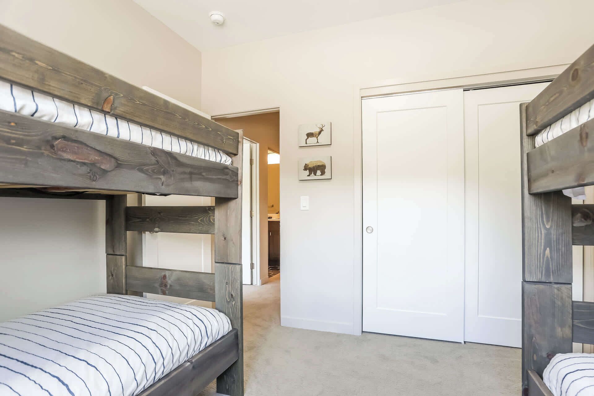 Una habitación con literas, una puerta blanca y dos cuadros con motivos de animales.